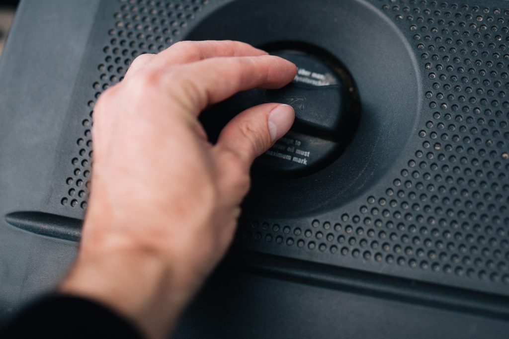 Een hand draait de olievuldop van een motor open