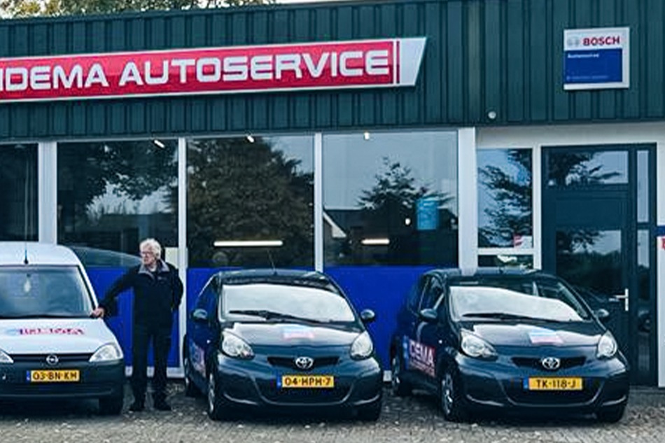 Het bord Idema Autoservice boven de pui, met een bestelbus en twee personenauto's ervoor
