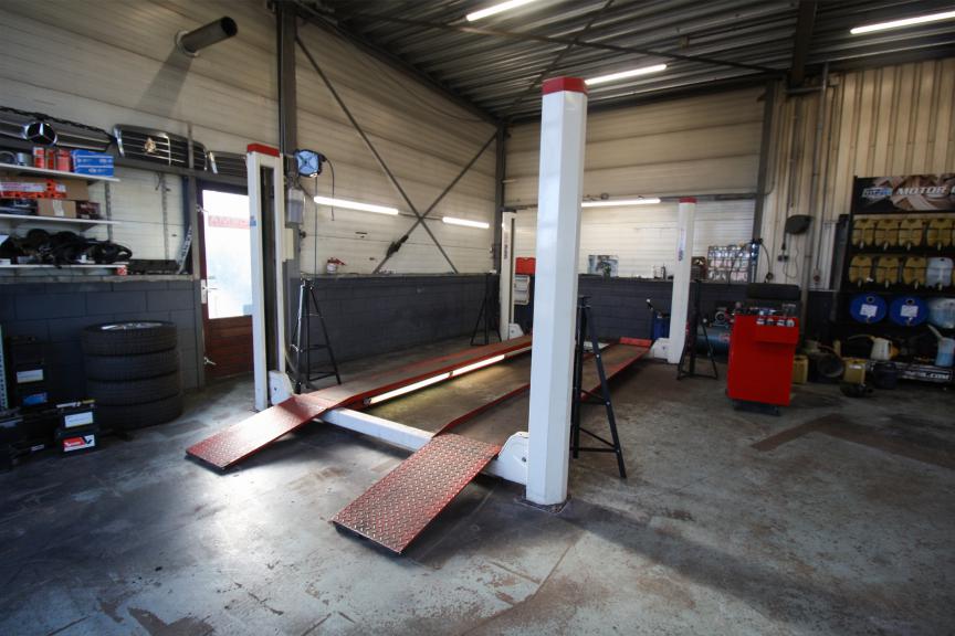 De werkplaats van Idema Autoservice met een vierkolomsbrug en een stapel banden